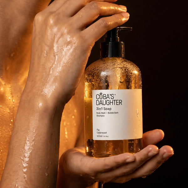 Bottle of CoBa's Daughter 3in1 Soap Fig & Cedarwood held in a hand against a dark background and glowing skin