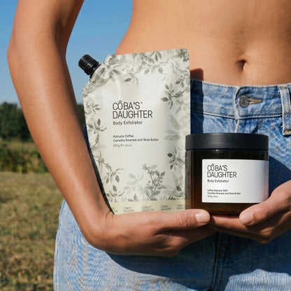 A woman wearing jeans holding CoBa's Daughter coffee scrub jar and refill pouch