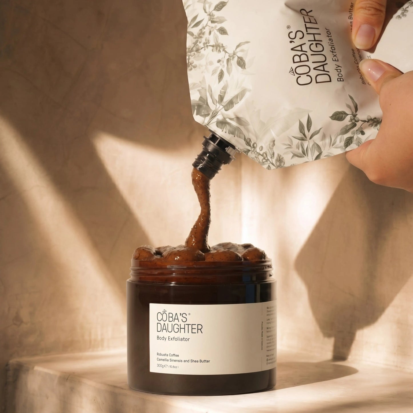 CoBa's Daughter coffee body scrub being poured into a jar with a hand holding a refill pouch.