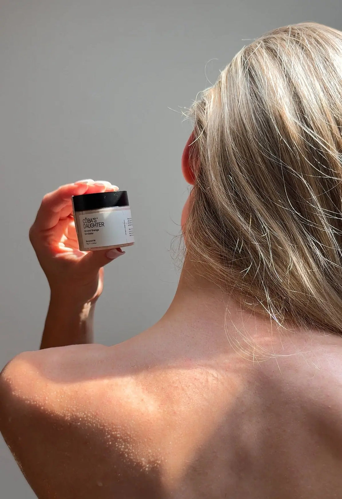 Woman showing her back and holding CoBa's Daughter 99% Pure Aloe Soothing Gel jar — hydrating skincare for smooth radiant skin
