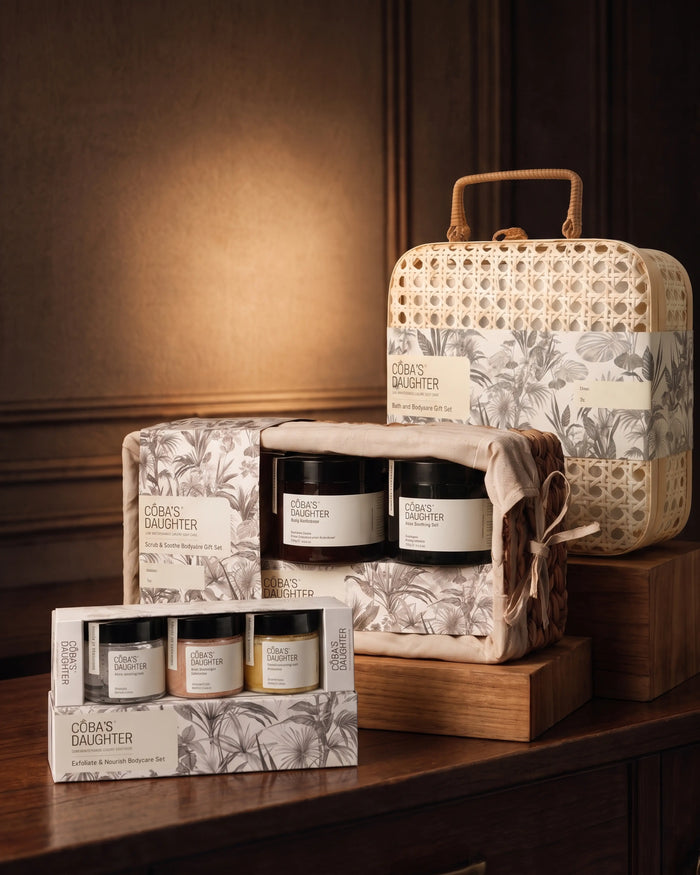 CoBa’s Daughter body care gift sets with a rattan case, scrub and aloe duo, and boxed mini trio on a wooden table.