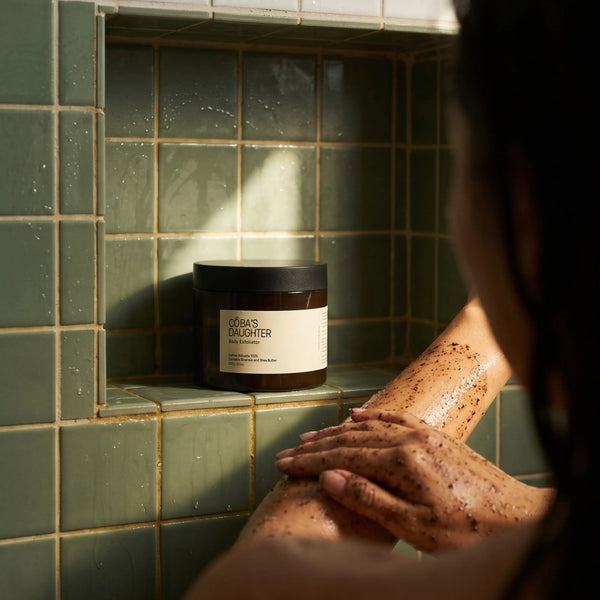A woman applying a CoBa's Daughter Coffee Body Scrub onto the shoulder in a spa-like atmosphere