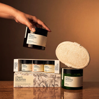 CoBa's Daughter body care products including coffee scrub, aloe gel, mini gift set, and a loofah on a wooden surface.
