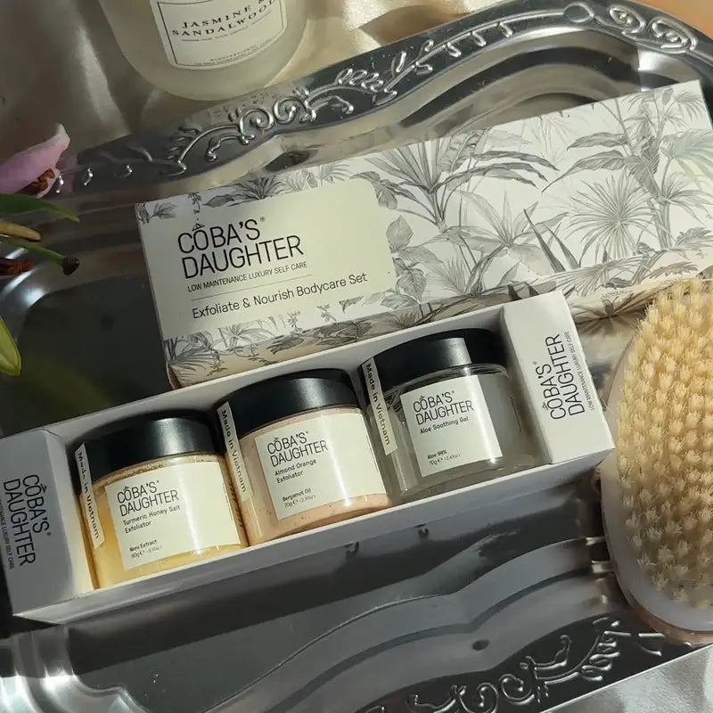 CoBa's Daughter Exfoliate and Nourish 3-Piece Body Care Gift Set in tropical botanical gift box with 2 mini scrubs and aloe gel jar, placed in a luxurious silver plate.