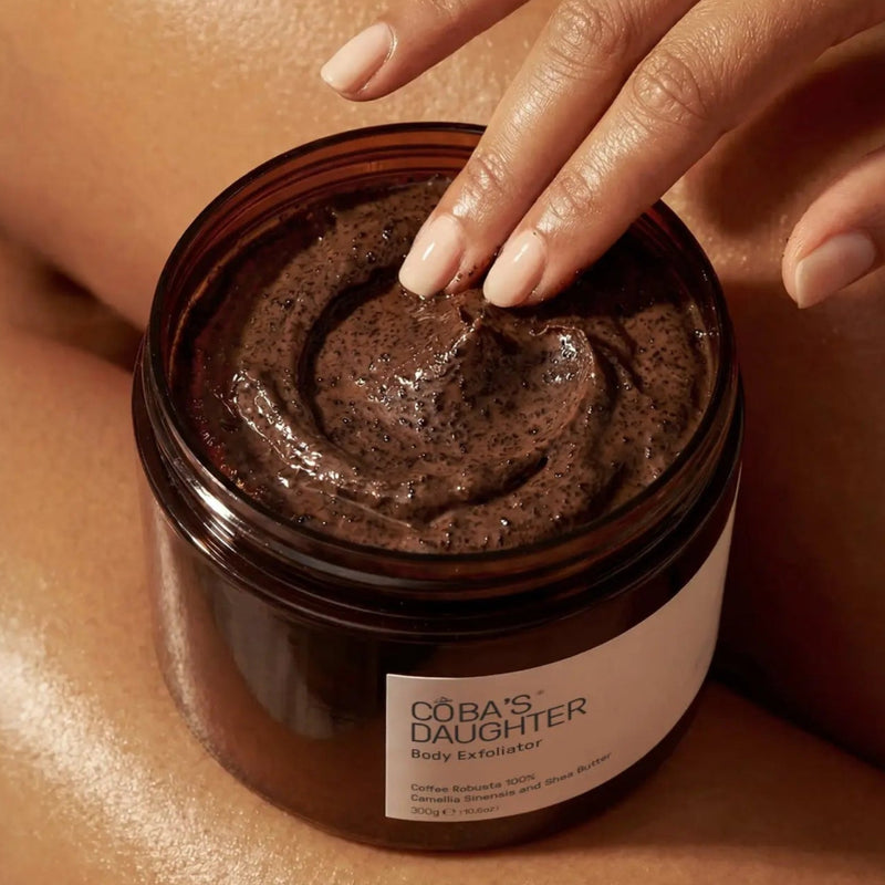 Scooping CoBa's Daughter Robusta Coffee Body Scrub from open jar showing dark brown finely milled texture with coffee grounds