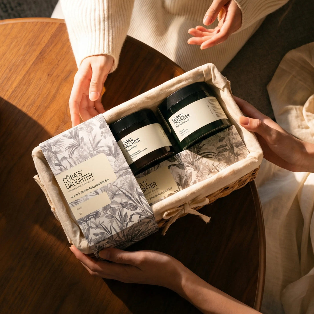 A person receiving a CoBa’s Daughter spa gift basket with coffee body scrub and aloe vera gel in a woven basket.